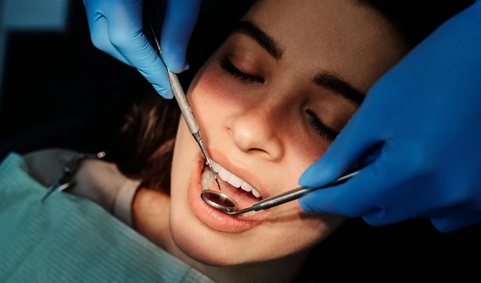 Dental examination in progress with gloved hands holding a mirror and instrument inside a patient's mouth.